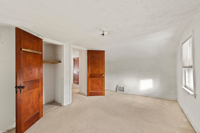 unfurnished bedroom featuring light colored carpet, a textured ceiling, and a closet