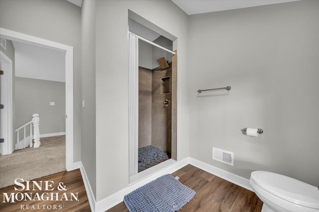 bathroom with hardwood / wood-style flooring, toilet, and a tile shower