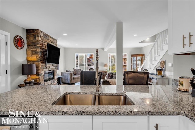 kitchen featuring white cabinets, a stone fireplace, and light stone counters