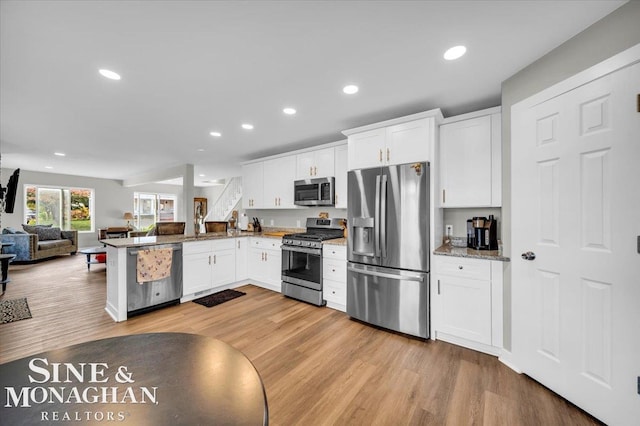 kitchen with stainless steel appliances, white cabinetry, kitchen peninsula, light stone counters, and light wood-type flooring