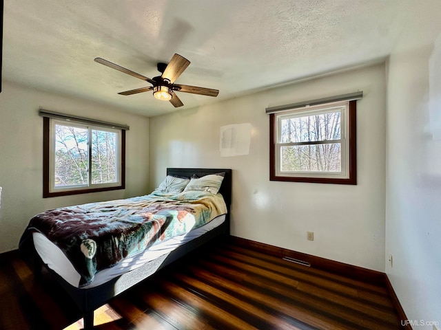 bedroom with a textured ceiling, dark hardwood / wood-style floors, multiple windows, and ceiling fan