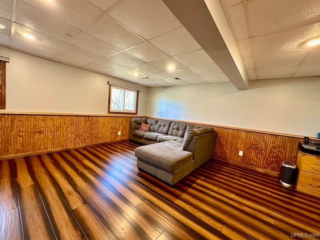 living room featuring a drop ceiling, dark wood-type flooring, and wooden walls