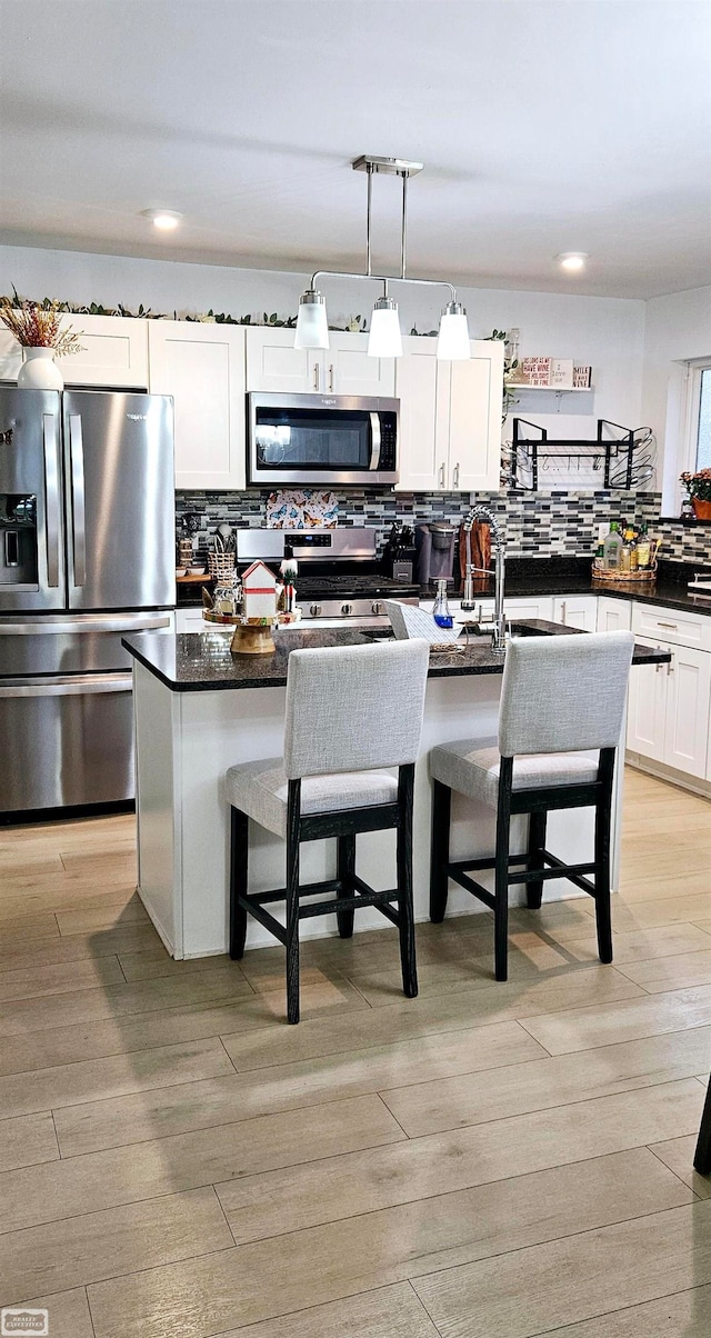 kitchen with a breakfast bar, sink, hanging light fixtures, appliances with stainless steel finishes, and a kitchen island with sink