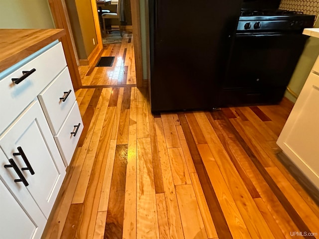 interior details featuring white cabinets, light wood-type flooring, and black range