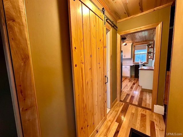 hall featuring a barn door, light hardwood / wood-style floors, wood ceiling, and ornamental molding