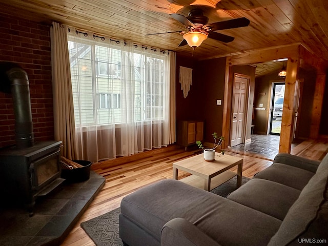 living room featuring a wood stove, light hardwood / wood-style floors, ceiling fan, and wood ceiling