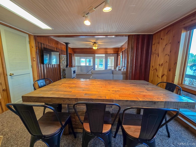 dining area featuring wood ceiling, a wood stove, wood walls, and ceiling fan