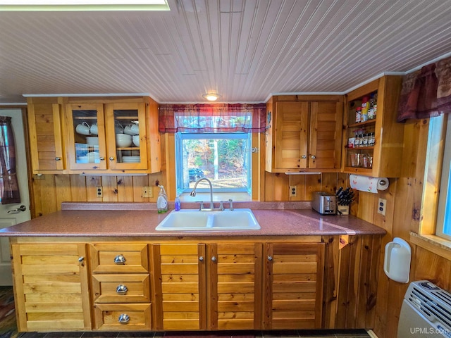 kitchen with wooden ceiling, a sink, glass insert cabinets, and wooden walls