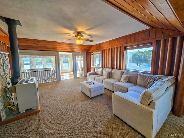 carpeted living area with ceiling fan, a healthy amount of sunlight, a wood stove, and wooden walls