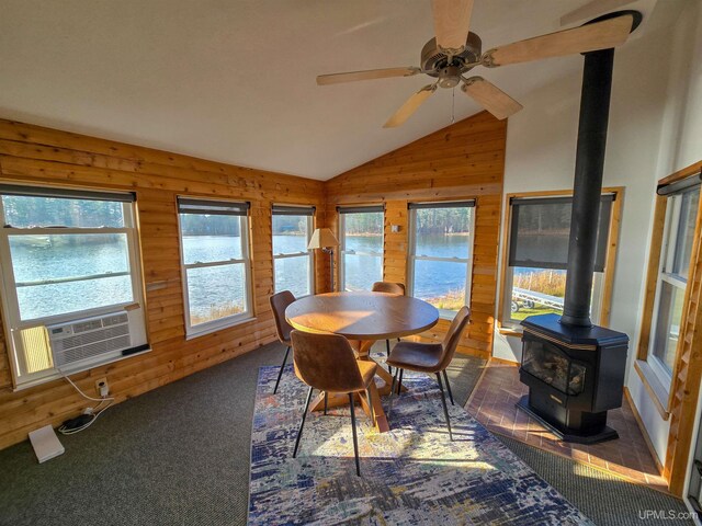 carpeted dining room featuring lofted ceiling, ceiling fan, a wood stove, cooling unit, and wood walls