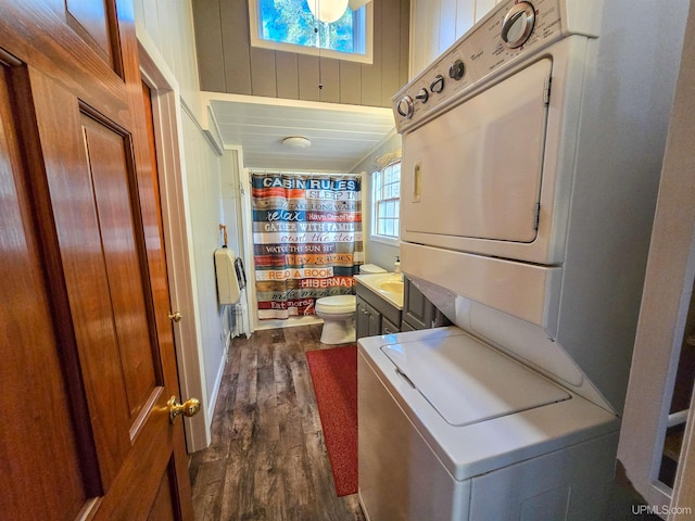 bathroom with toilet, wood walls, stacked washing maching and dryer, and wood finished floors