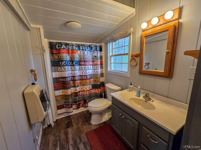 bathroom with heating unit, toilet, wood finished floors, vanity, and a shower with curtain