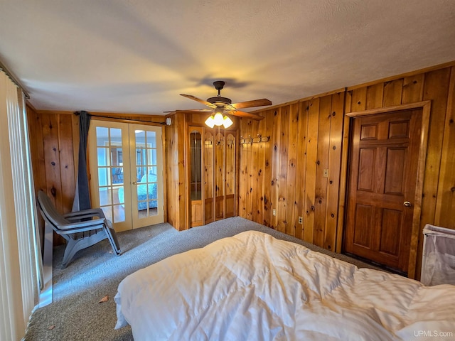 bedroom featuring access to exterior, carpet, french doors, ceiling fan, and wooden walls