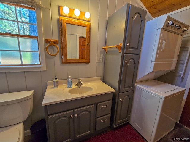 bathroom with stacked washer / dryer, vanity, toilet, and a decorative wall