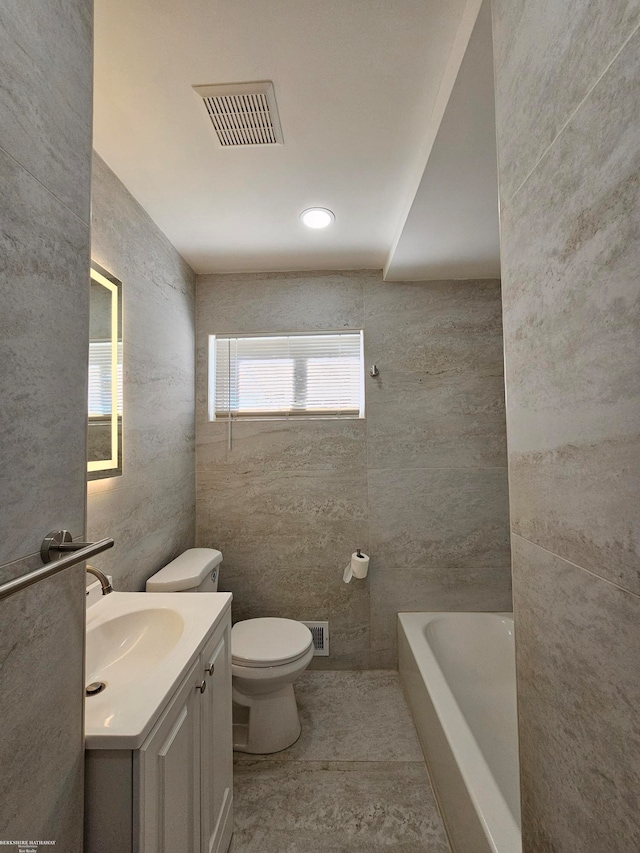 bathroom featuring toilet, vanity, a tub to relax in, and tile walls