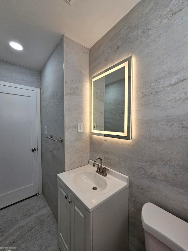 bathroom with vanity, toilet, and tile walls