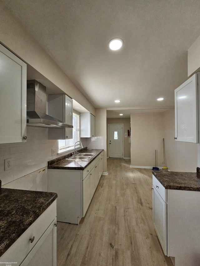 kitchen with wall chimney range hood, decorative backsplash, sink, light hardwood / wood-style floors, and white cabinets