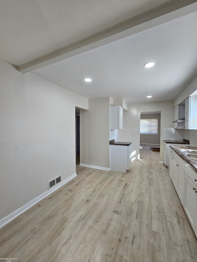 kitchen featuring white cabinetry, light wood-type flooring, and beamed ceiling