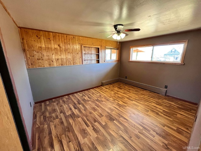 empty room featuring hardwood / wood-style flooring, ceiling fan, wooden walls, and a baseboard radiator