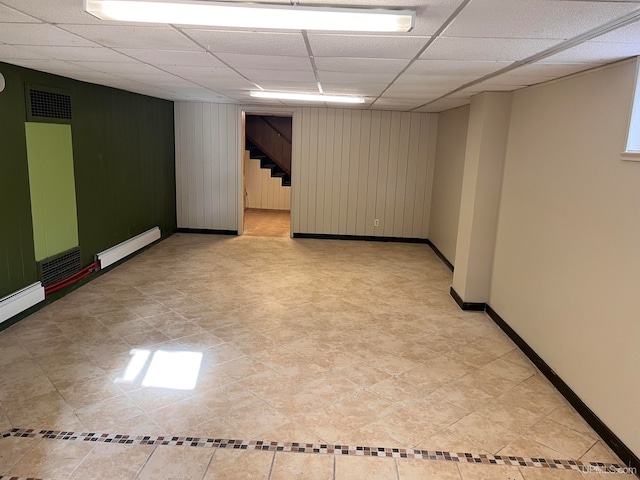 interior space featuring wood walls, a drop ceiling, and baseboard heating