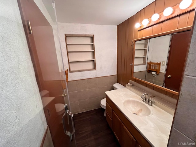 bathroom featuring wood-type flooring, vanity, built in features, toilet, and tile walls