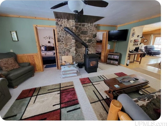 living room with a wood stove, light colored carpet, ceiling fan, and crown molding