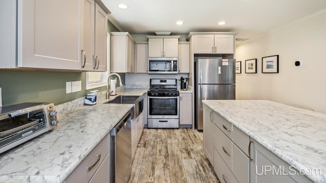 kitchen featuring stainless steel appliances, light hardwood / wood-style flooring, light stone counters, and ornamental molding