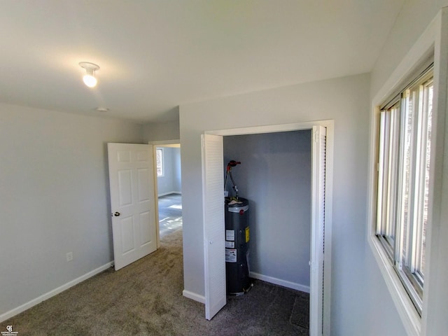 unfurnished bedroom with water heater, a closet, and dark colored carpet