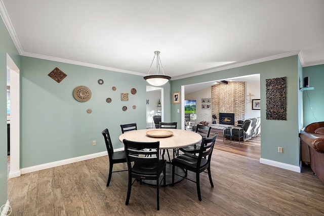 dining space with a fireplace, wood-type flooring, and crown molding