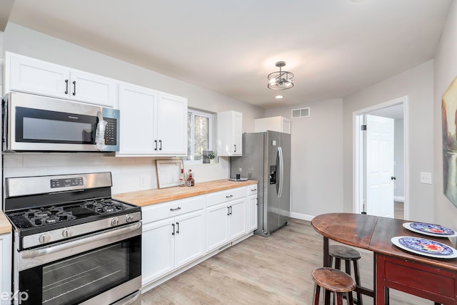 kitchen with appliances with stainless steel finishes, light wood-type flooring, white cabinets, butcher block countertops, and decorative backsplash