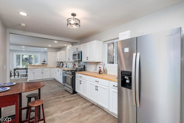 kitchen with wooden counters, stainless steel appliances, white cabinets, decorative backsplash, and light hardwood / wood-style flooring