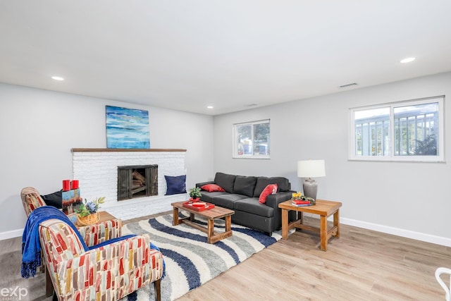 living room with light wood-type flooring, a healthy amount of sunlight, and a brick fireplace