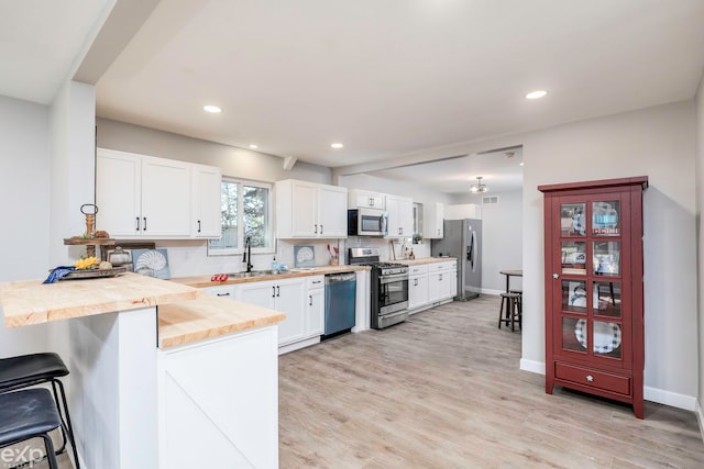 kitchen with kitchen peninsula, appliances with stainless steel finishes, a breakfast bar area, light hardwood / wood-style flooring, and white cabinets