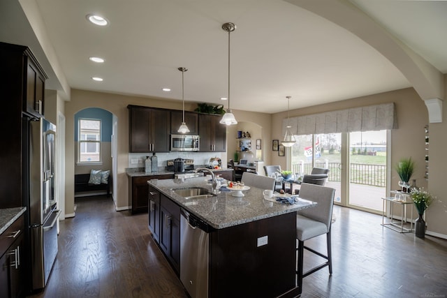 kitchen with light stone countertops, a kitchen breakfast bar, arched walkways, stainless steel appliances, and a sink