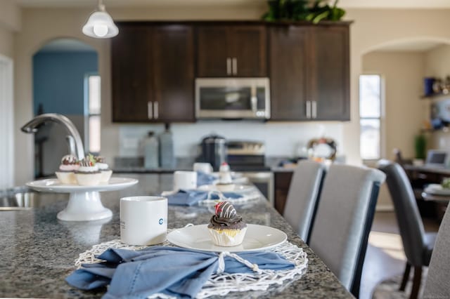 kitchen with stainless steel microwave, dark brown cabinets, arched walkways, and stone countertops