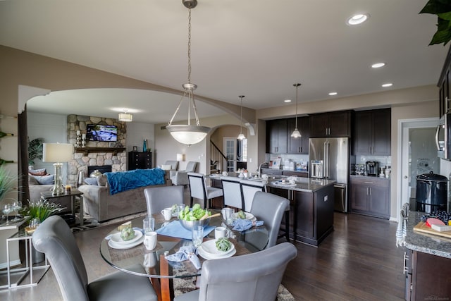 dining space featuring recessed lighting, arched walkways, dark wood-style flooring, stairs, and a stone fireplace