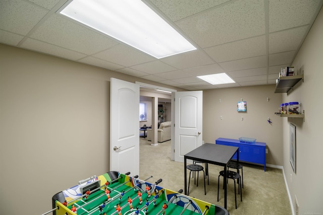 rec room featuring light carpet, a drop ceiling, and baseboards