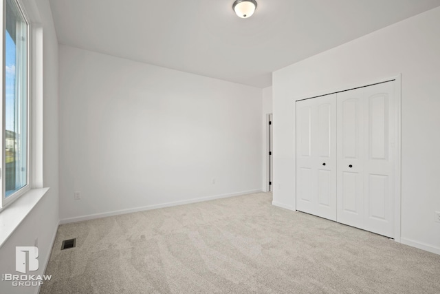 unfurnished bedroom featuring a closet, multiple windows, and light colored carpet