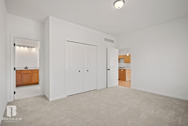 unfurnished bedroom with light colored carpet, sink, connected bathroom, and a closet