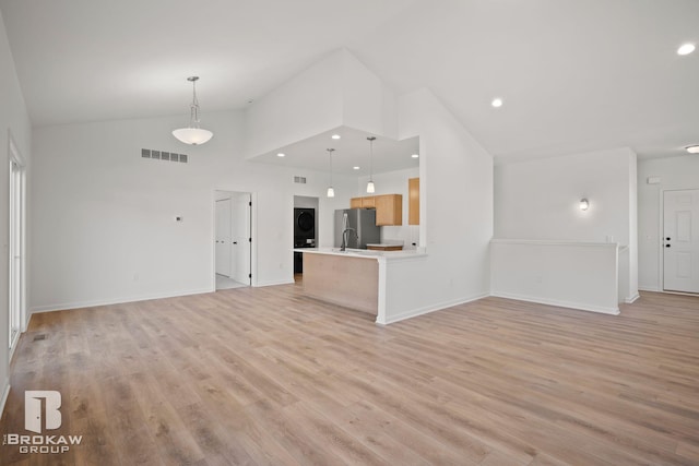 unfurnished living room with sink, light wood-type flooring, and high vaulted ceiling