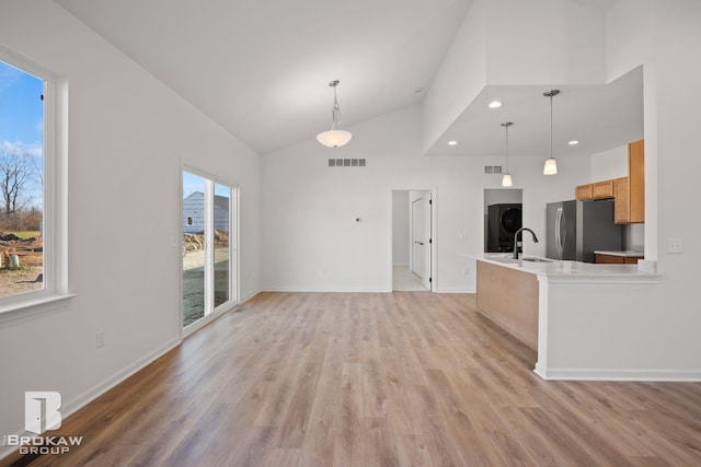 unfurnished living room with high vaulted ceiling, a wealth of natural light, sink, and light hardwood / wood-style floors