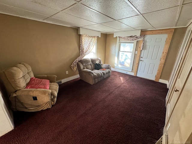 living area with a drop ceiling and dark colored carpet