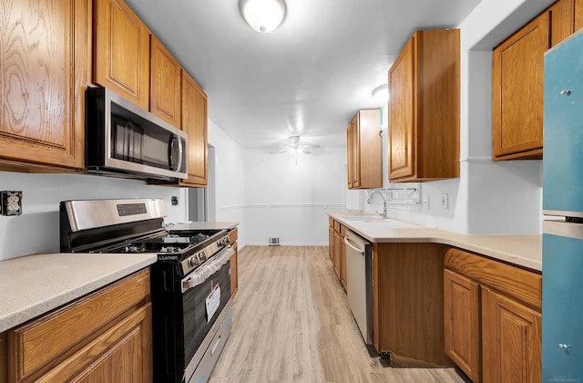 kitchen with appliances with stainless steel finishes, light hardwood / wood-style floors, ceiling fan, and sink