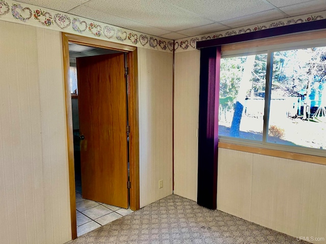 empty room featuring a paneled ceiling, wooden walls, and light carpet