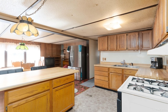 kitchen with a textured ceiling, light carpet, sink, white gas stove, and stainless steel fridge