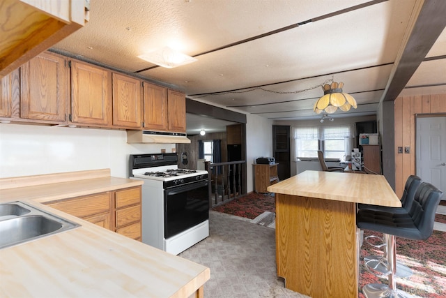 kitchen featuring white range with gas cooktop, a kitchen bar, a textured ceiling, a kitchen island, and wood counters