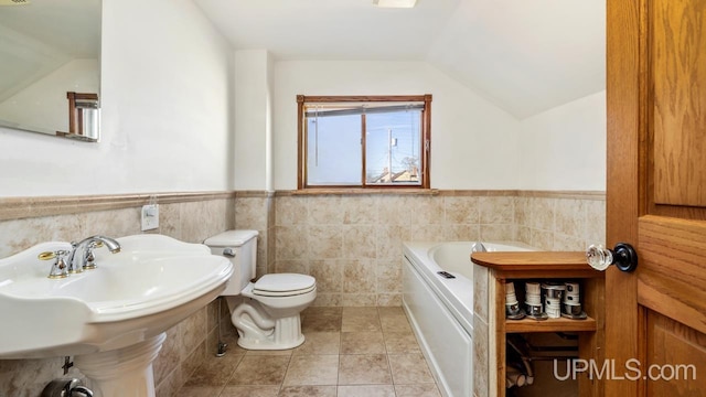 bathroom featuring tile patterned flooring, vaulted ceiling, a bathing tub, toilet, and tile walls