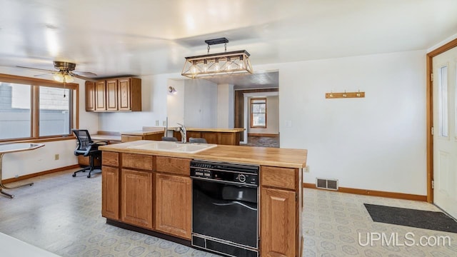 kitchen featuring a center island with sink, decorative light fixtures, black dishwasher, sink, and ceiling fan