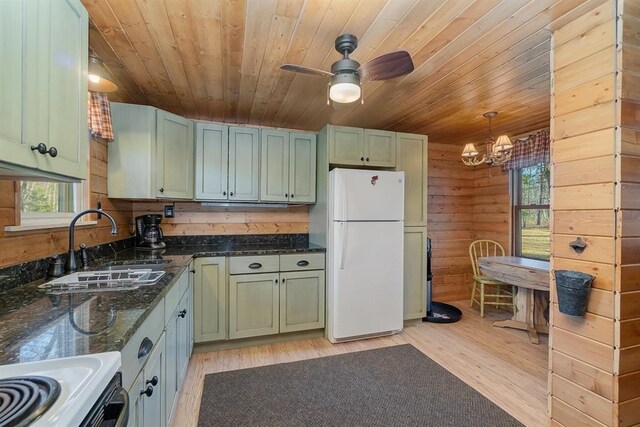 kitchen with sink, white refrigerator, dark stone counters, decorative light fixtures, and wooden walls