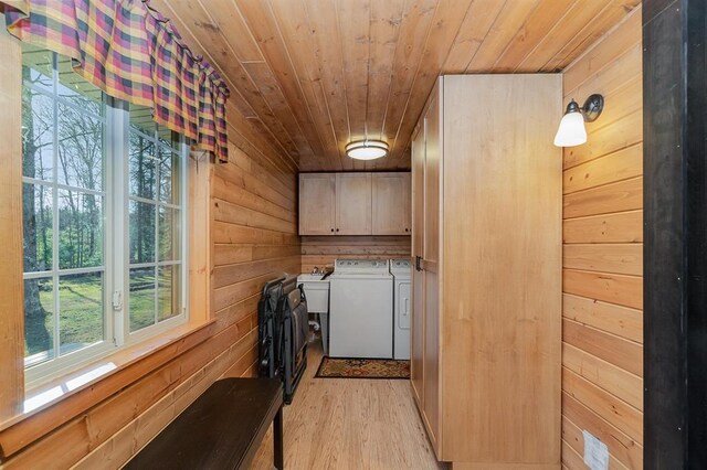 laundry room with separate washer and dryer, wooden walls, cabinets, and plenty of natural light